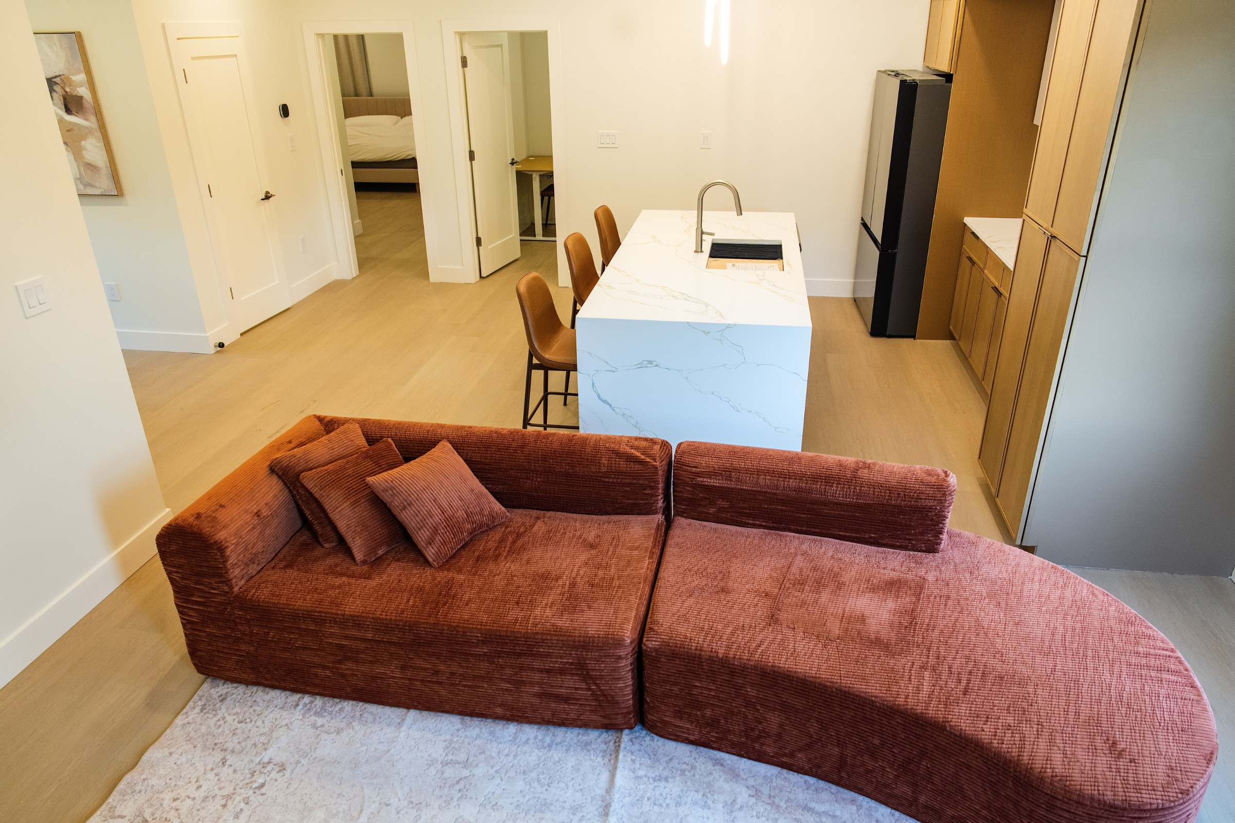 Curved rust sectional on pale rug with kitchen island beyond.