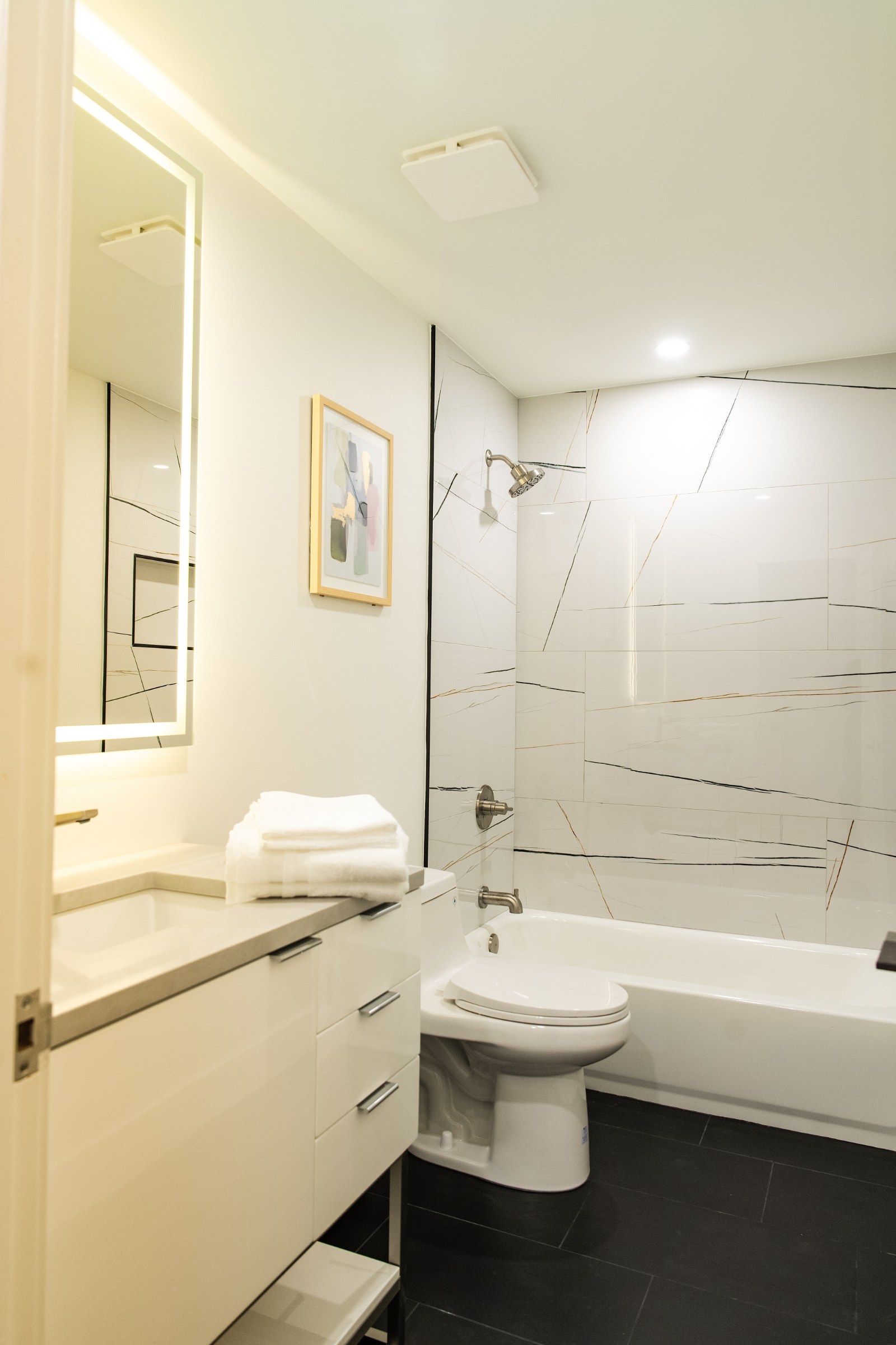 Soaker tub with veined marble surround and dark tile floor.